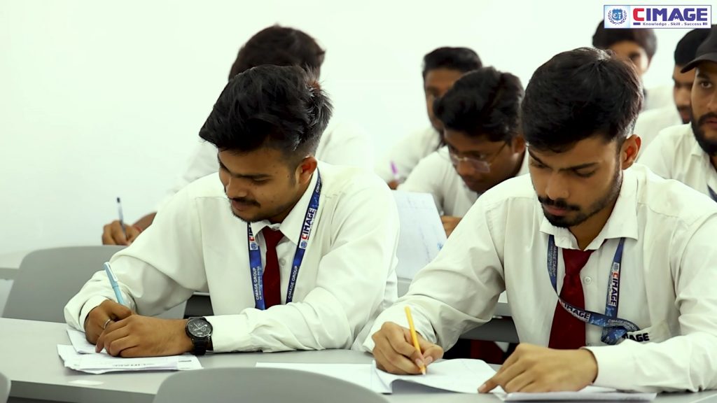 Several students are seated at desks in a classroom, attentively writing in notebooks.
