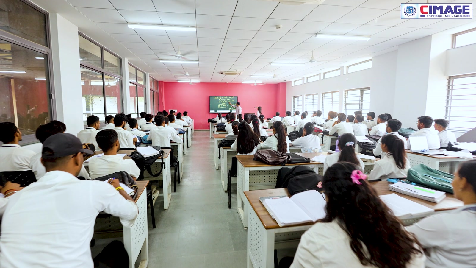 Students sitting in rows at desks inside a classroom listening to a lecture.