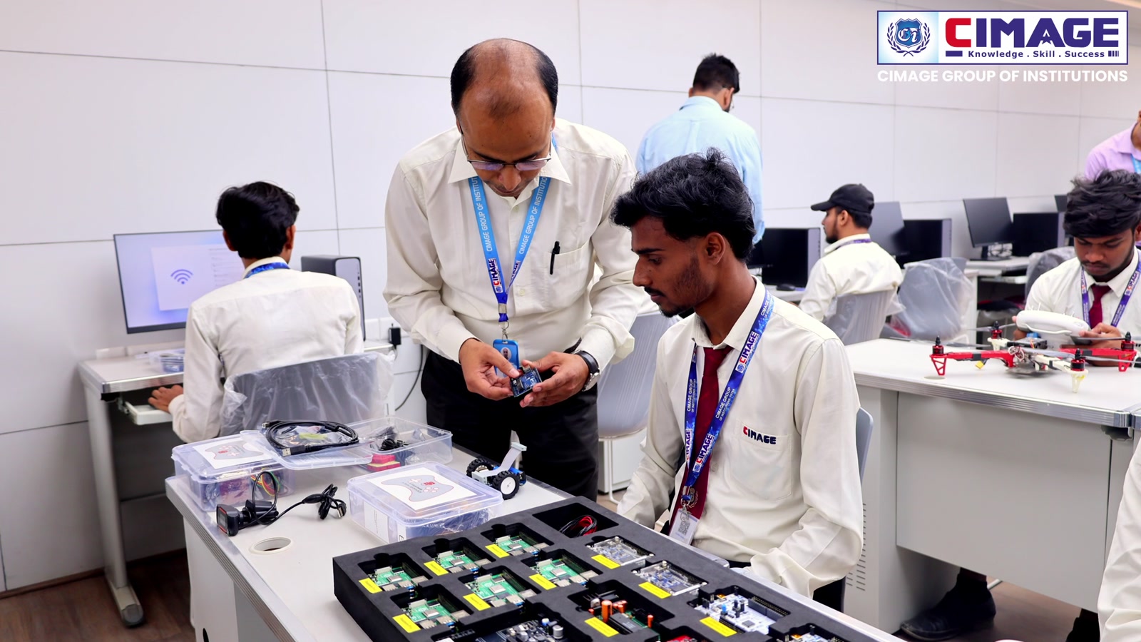 A faculty member assists a student working with electronic parts and equipment at a desk.