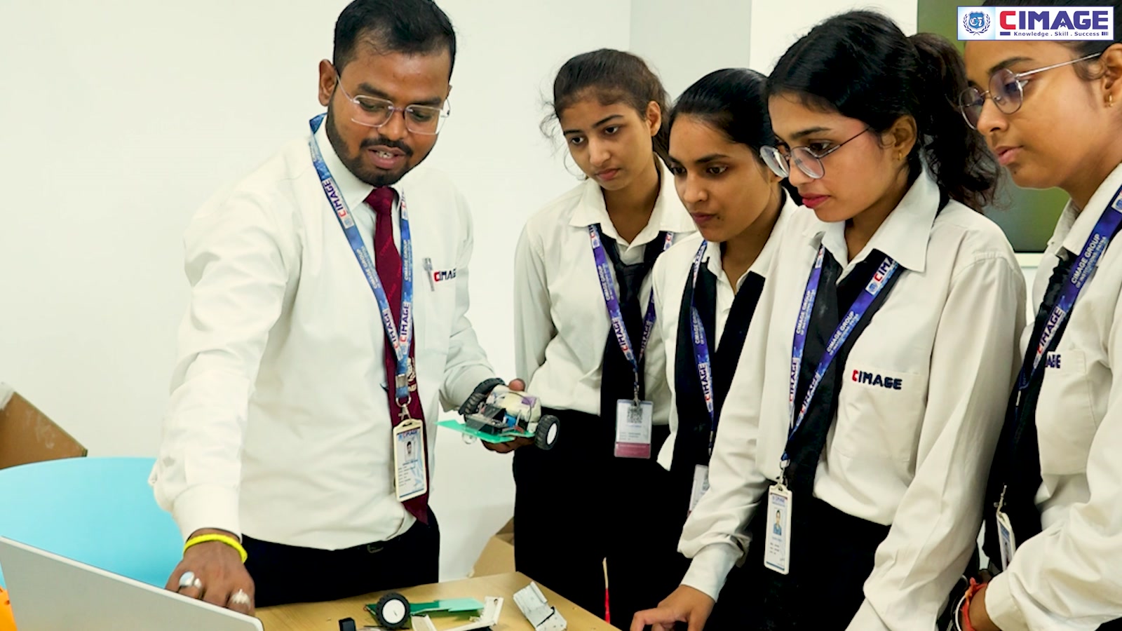Faculty member guiding four students around a table with electronic components in a lab.