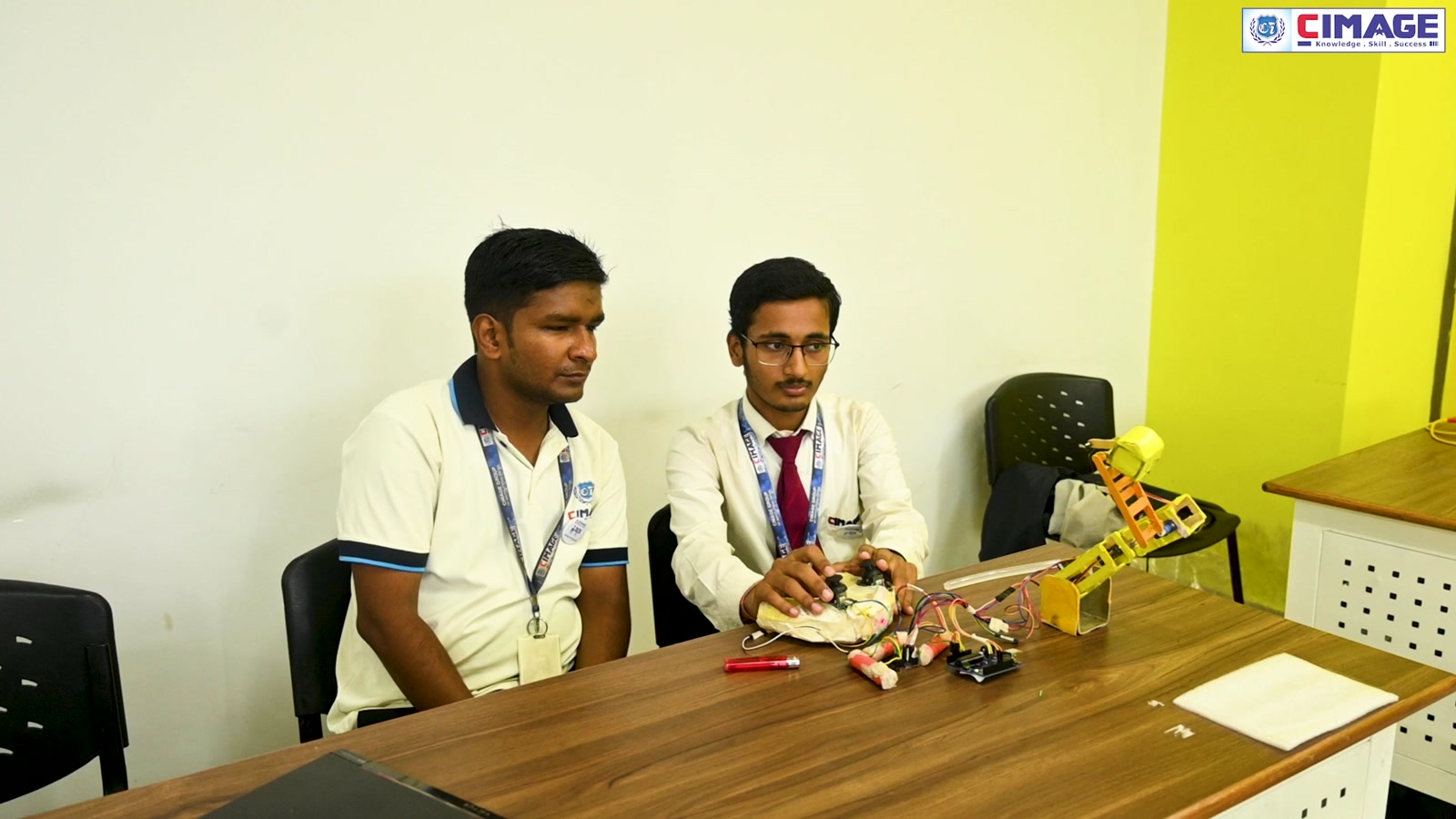 Two students sit at a table working with mechanical parts and robotics equipment.