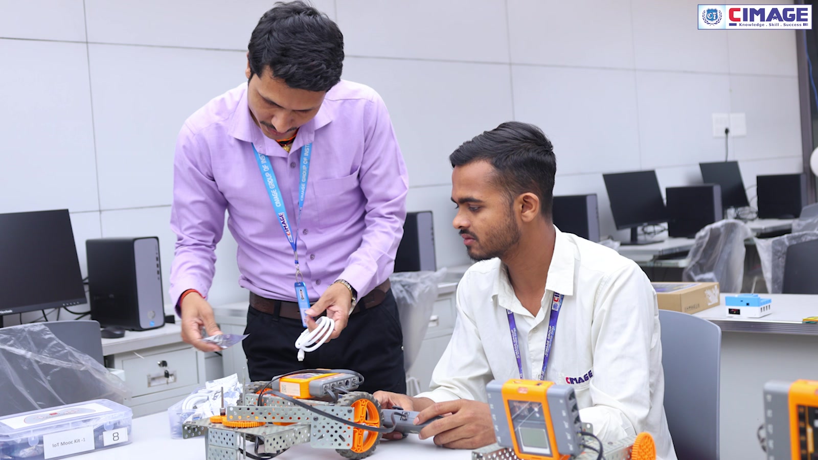 A faculty member helping a student assemble robotics parts on a workbench in a lab.
